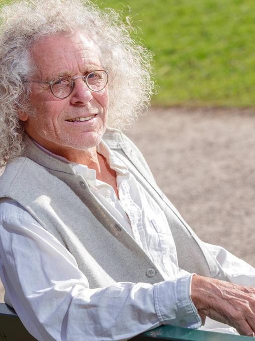 Rainer Langhans sitzt in München auf einer Parkbank und lächelt für eine Foto.