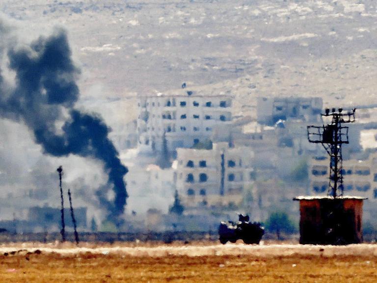 Leicht verschwommene Aufnahme mehrerer Gebäude in Kobane, aus denen Rauch aufsteigt.