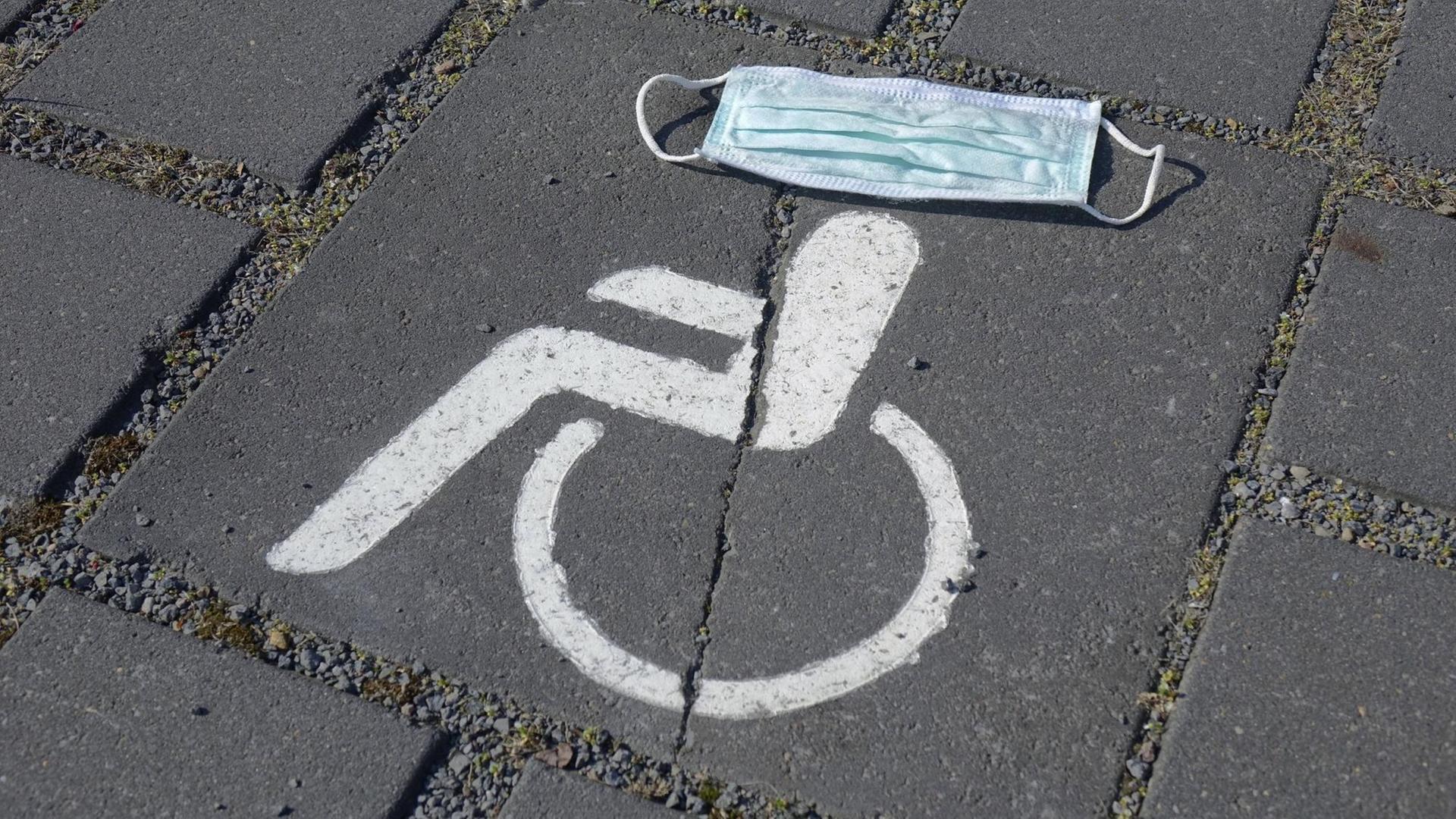 Symbol eines Behindertenparkplatzes, darüber ein Mundschutz