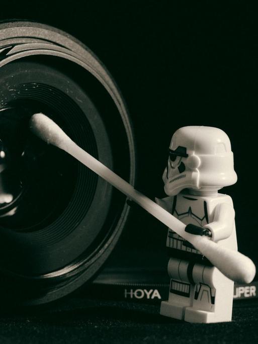 Eine Legofigur hält reinigt mit einem Wattestäbchen ein Kameraobjektiv