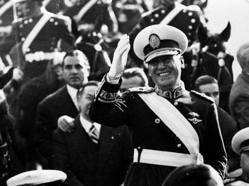 Der argentinische Präsident Juan Domingo Perón, uniformiert auf einer Militärparade, den Zusachuern mit der rechten Hand zuwinkend.