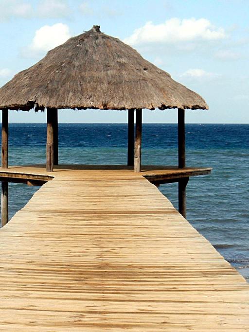 Ein Holzsteg, am Ende mit einer kleinen Hütte, führt aufs Meer