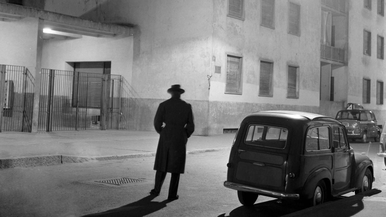 Nächtliche Straßenansicht mit der Silhouette eines Mannes in langem Mantel und Hut, der nach Agent oder Detektiv aussieht