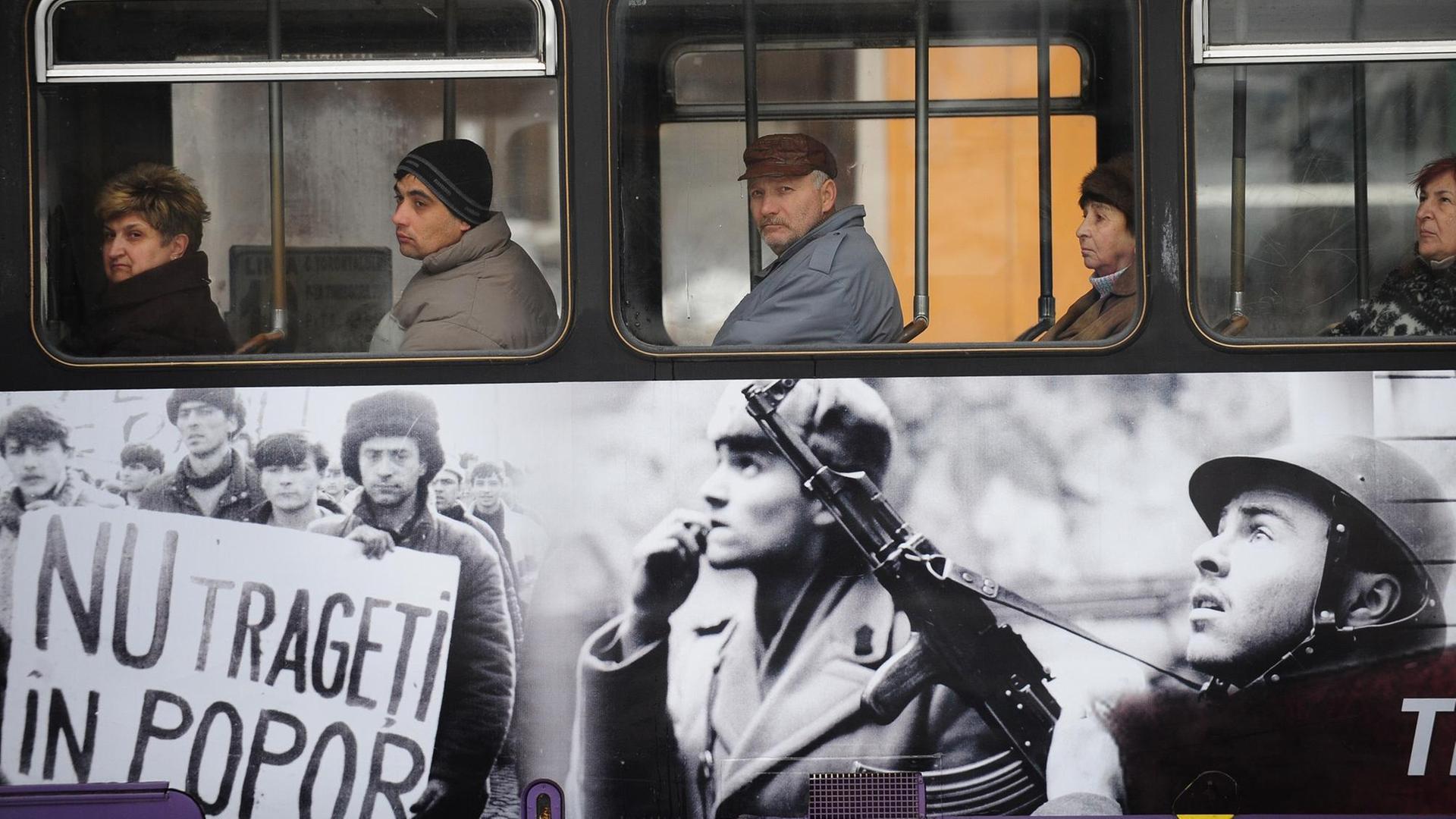 Fahrgäste sitzen in einer Straßenbahn in Timișoara, die mit Fotos der Rumänischen Revolution 1989 beklebt ist