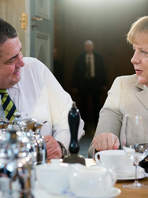 Bundeskanzlerin Angela Merkel (CDU) und Wirtschaftsminister Sigmar Gabriel (SPD) sitzen an einem Tisch und schauen sich an.