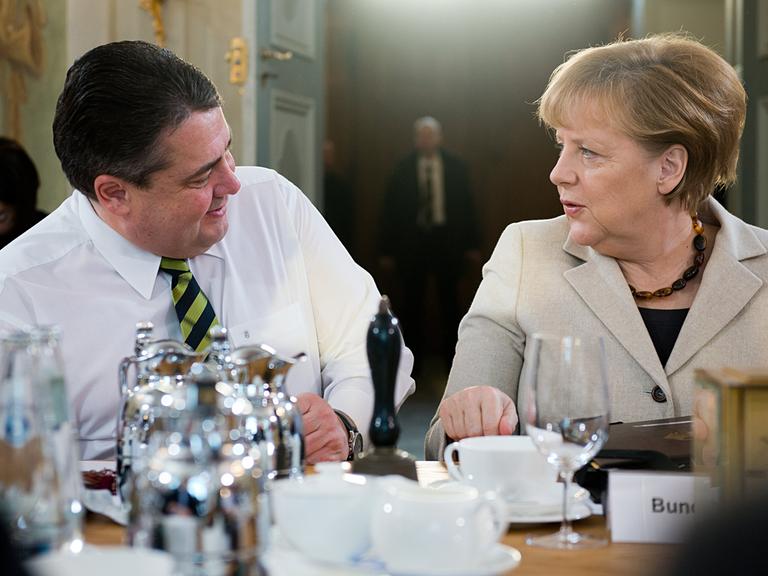 Bundeskanzlerin Angela Merkel (CDU) und Wirtschaftsminister Sigmar Gabriel (SPD) sitzen an einem Tisch und schauen sich an.