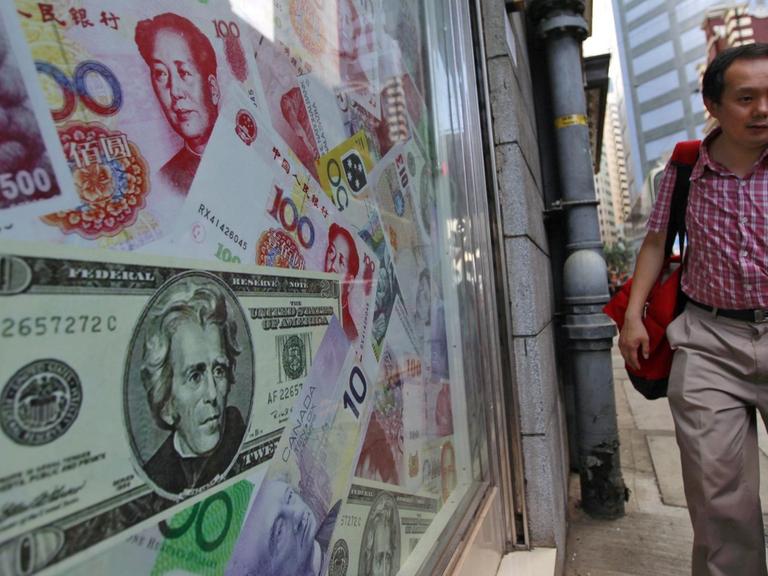 In einem Schaufenster in Hongkong sind Yuan- und Dollar-Scheine zu sehen, ein Mann geht vorbei.