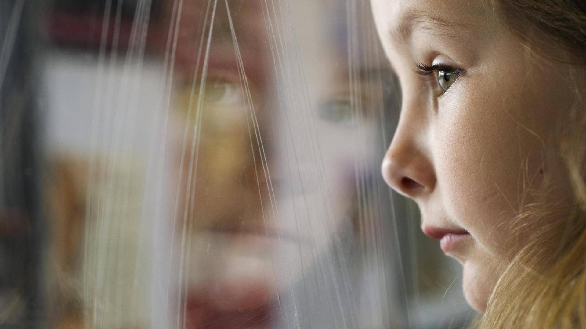 Ein junges Mädchen lehnt sich an die Glasscheibe eines Zugfensters.