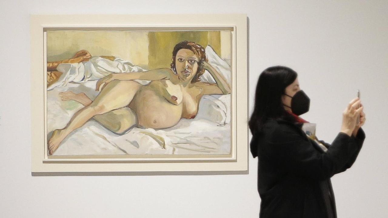 Blick in die Ausstellung. Eine Frau steht neben dem Gemälde "Pregnant Maria" von Alice Neel.