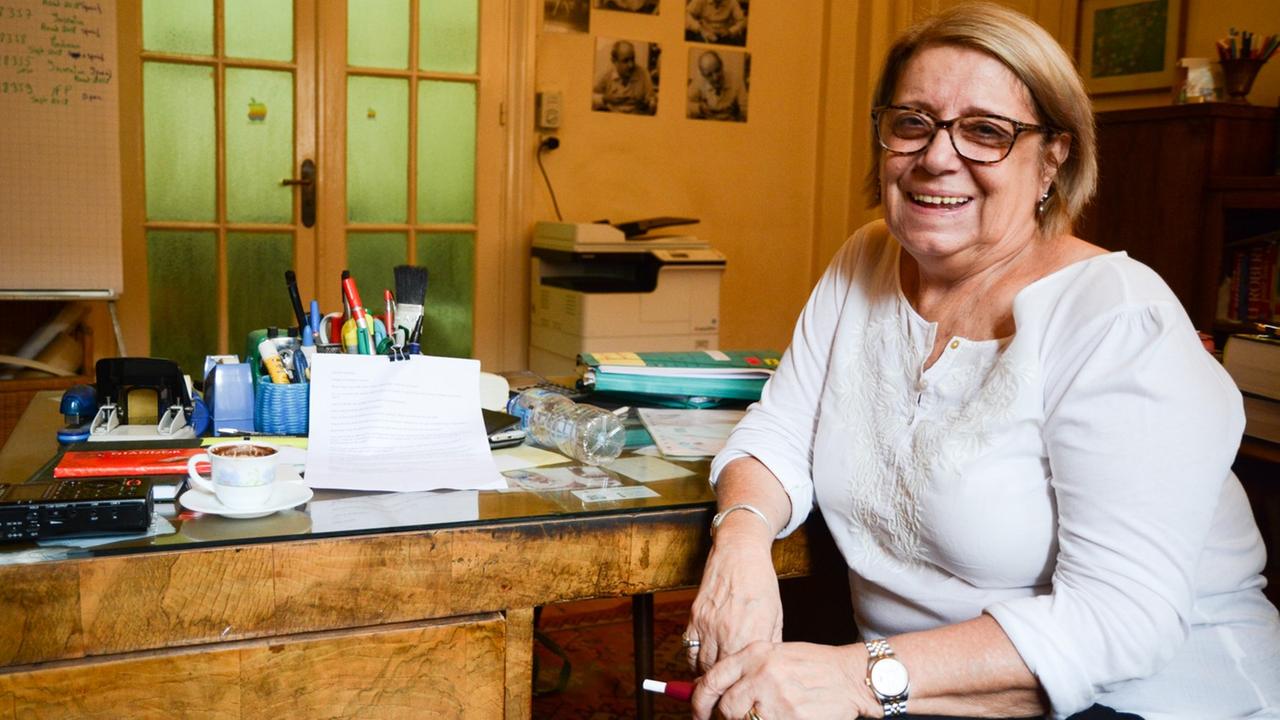 Eine Frau in weißem Oberteil und mit Brille schaut lächelnd in die Kamera.