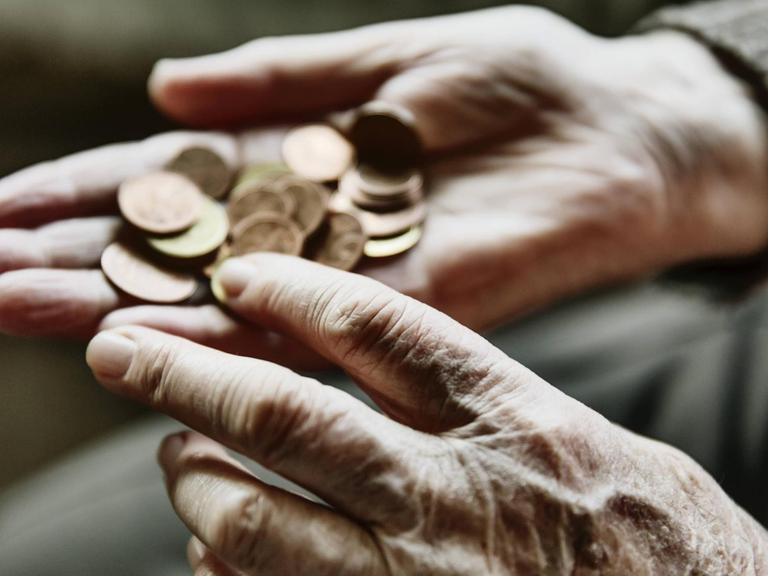 Nahaufnahme der Hand einer alten Frau, die ein paar Münzen zählt.