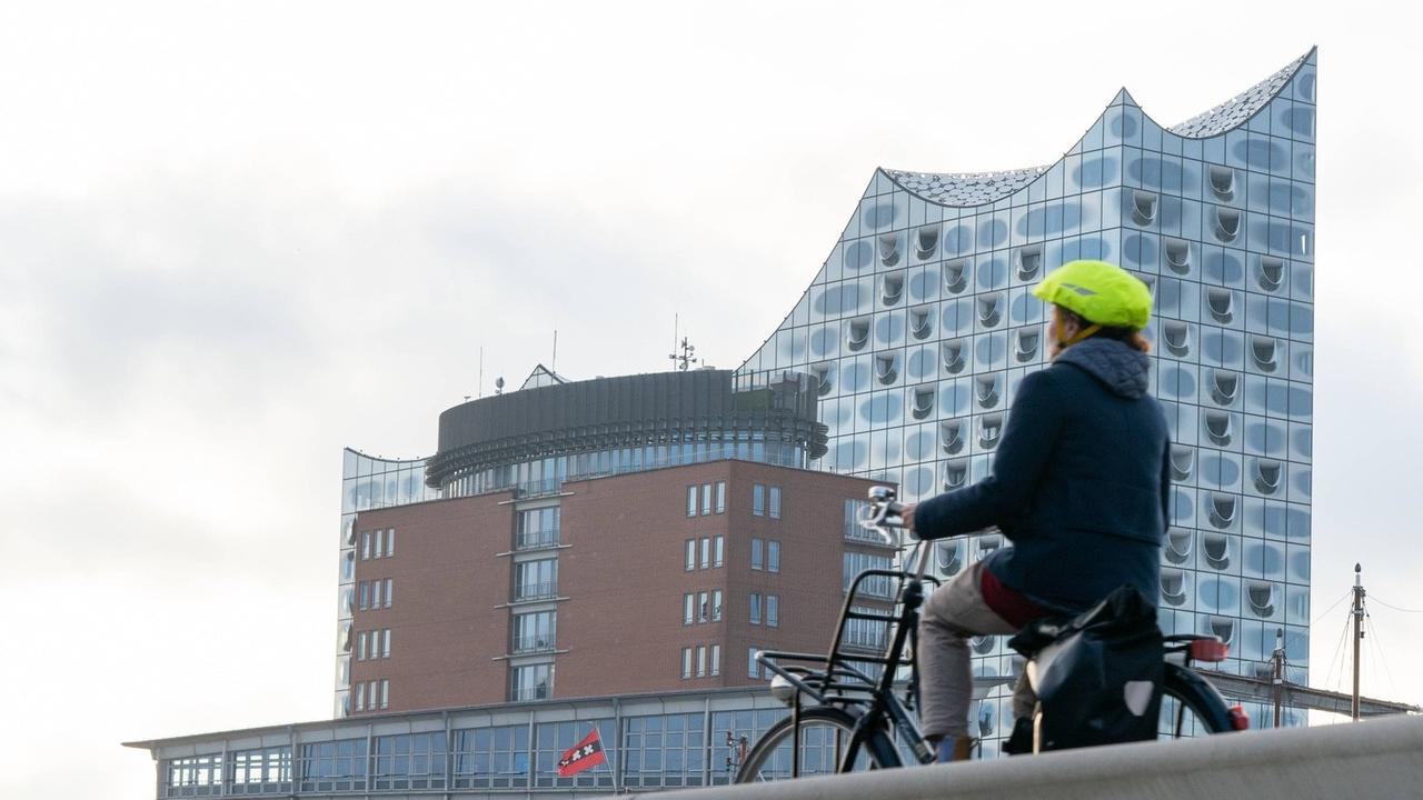 Eine fahrende Radfahrerin mit Helm ist von hinten zu sehen, im Hintergrund die Elbphilharmonie.