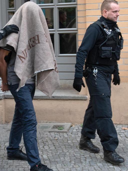 Zwei Polizisten führen einen verdächtigen Mann nach einer Razzia gegen kriminelle Mitglieder arabischer Großfamilien in Berlin ab.
