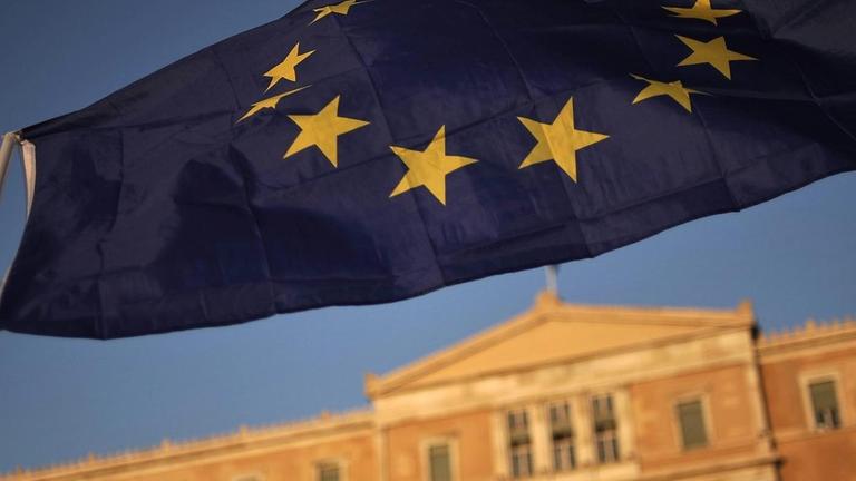 Eine Hand schwenkt eine EU-Fahne vor dem griechischen Parlament in Athen.