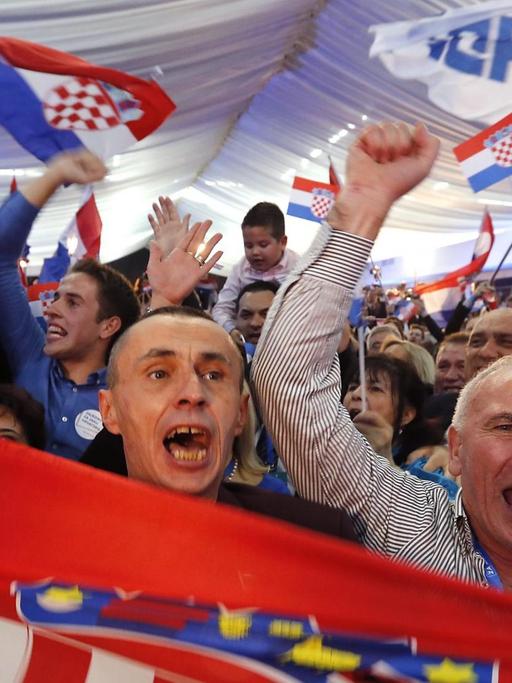 Jubelnde Anhänger der kroatischen Partei HDZ schwenken ein Wahlplakat