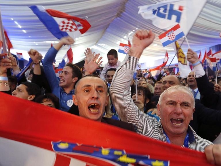 Jubelnde Anhänger der kroatischen Partei HDZ schwenken ein Wahlplakat
