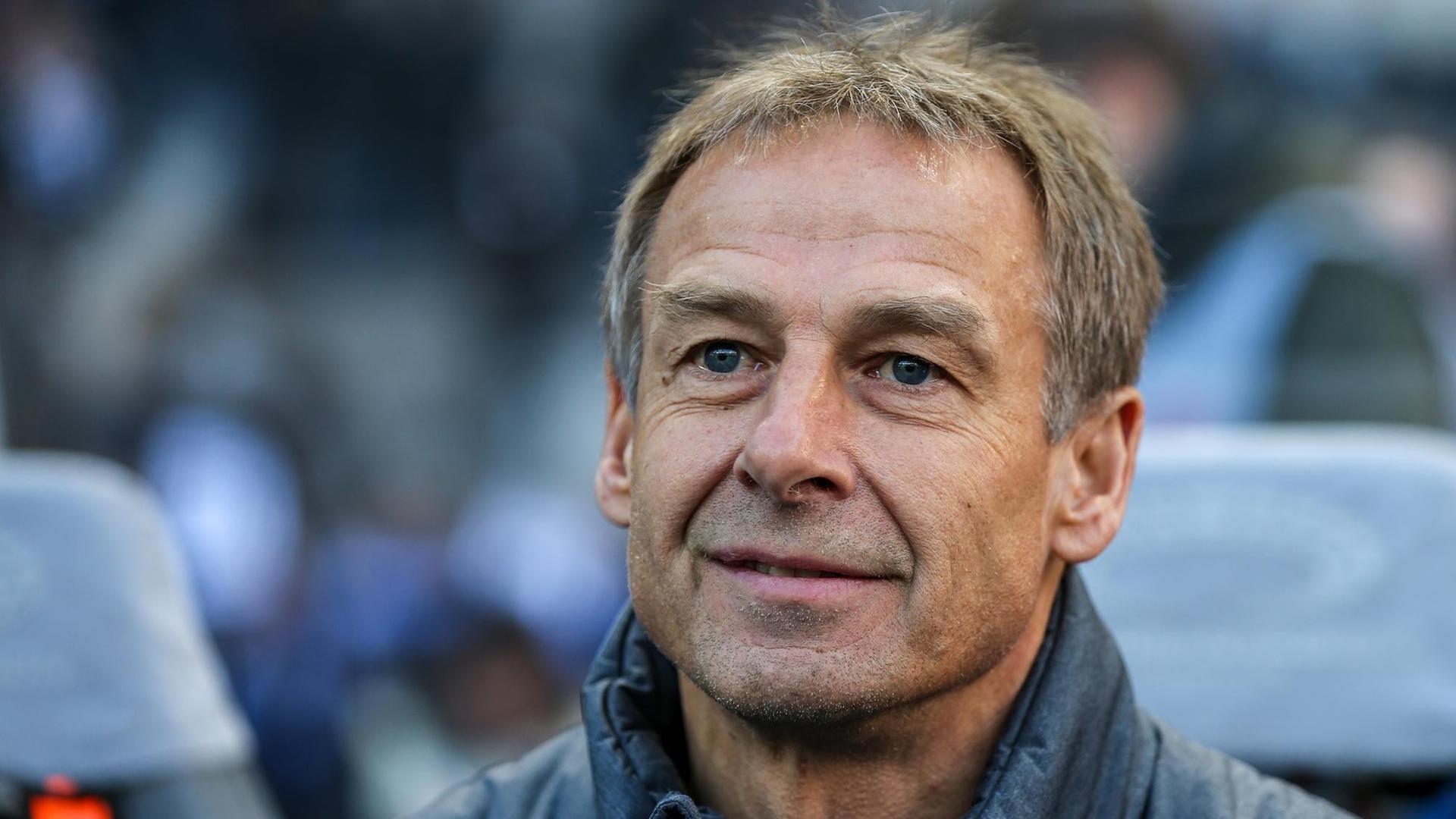 Auf dem Bild ist Jürgen Klinsmann. Er steht nehmen einem Fußball-Feld. 