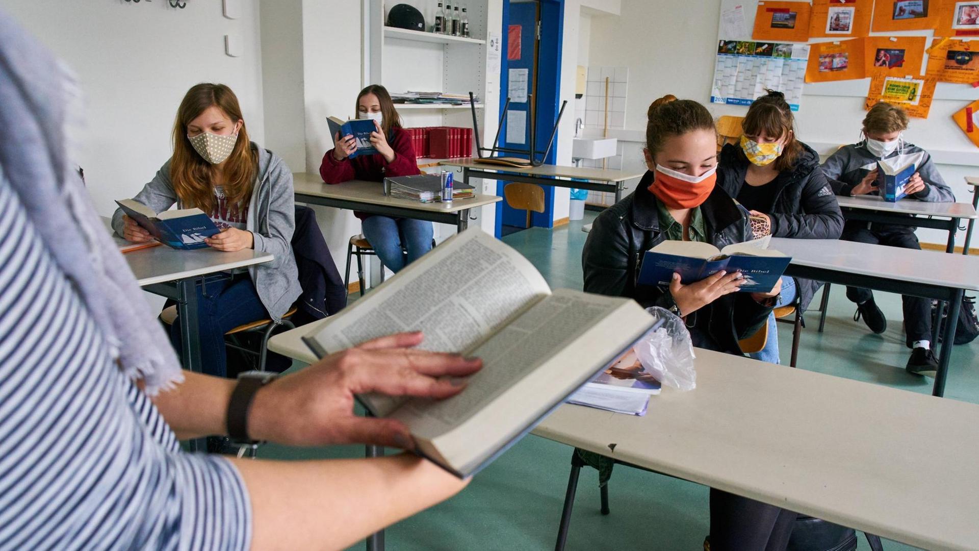 Schülerinnen und Schüler mit Masken sitzen an ihren Tischen im Klassenraum und lesen im Unterricht in Marktoberdorf im 27. April 2020.