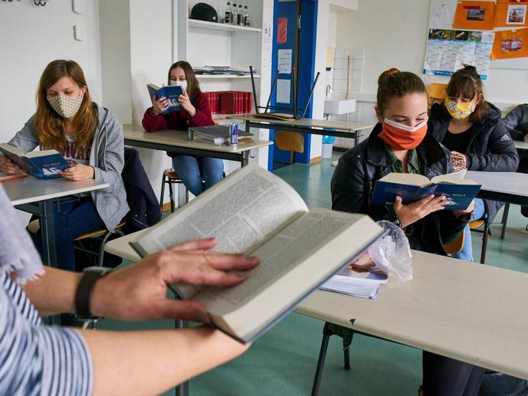 Schülerinnen und Schüler mit Masken sitzen an ihren Tischen im Klassenraum und lesen im Unterricht in Marktoberdorf im 27. April 2020.