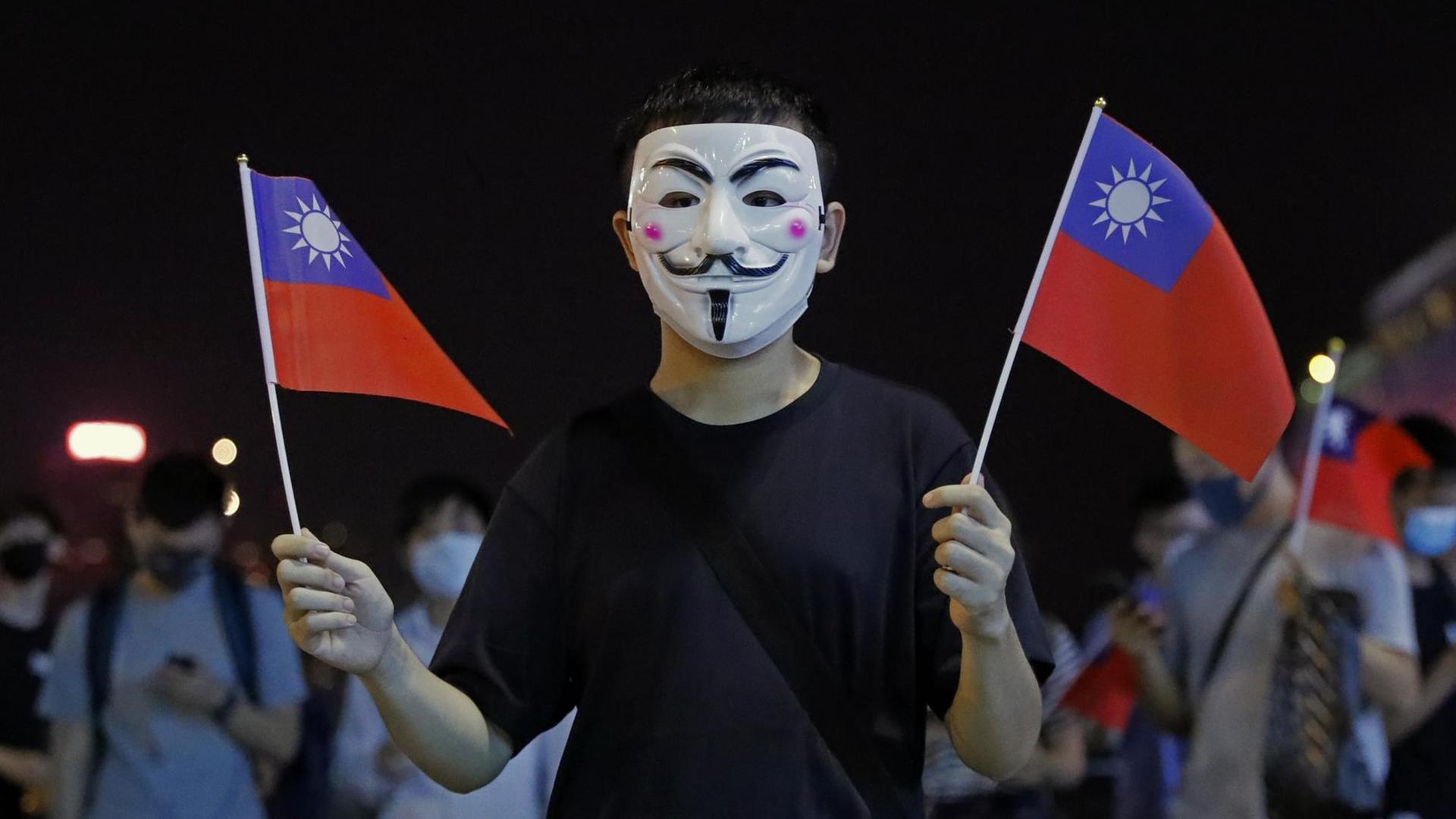 Ein maskierter Mann hält in beiden Händen kleine Taiwan-Flaggen