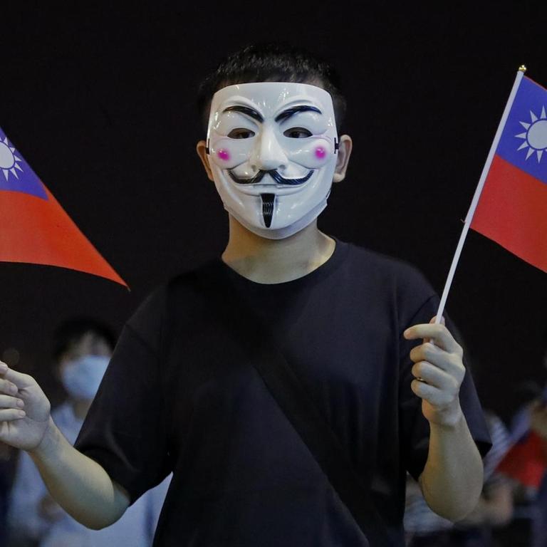 Ein maskierter Mann hält in beiden Händen kleine Taiwan-Flaggen