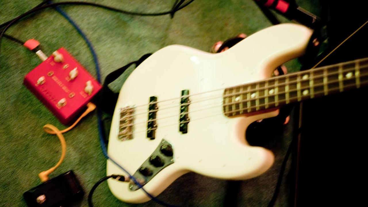 Ein weißer E-Bass (Modell Fender Jazz Bass) steht neben einem Effektgerät.
