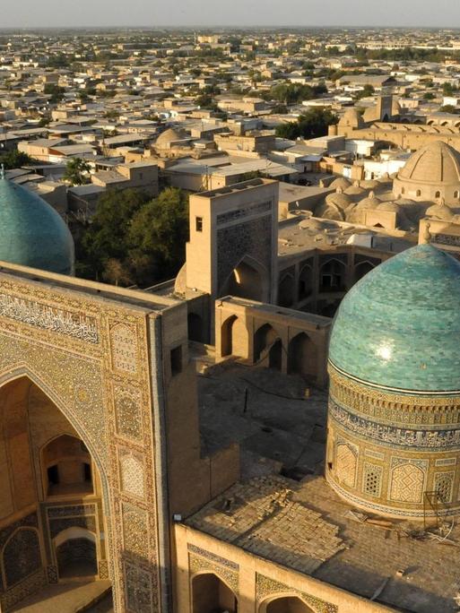 Blick auf die blauen Kuppeln und den großen Iwan der islamischen Lehrstätte Mir-i Arab Madrasa in Usbekistan.