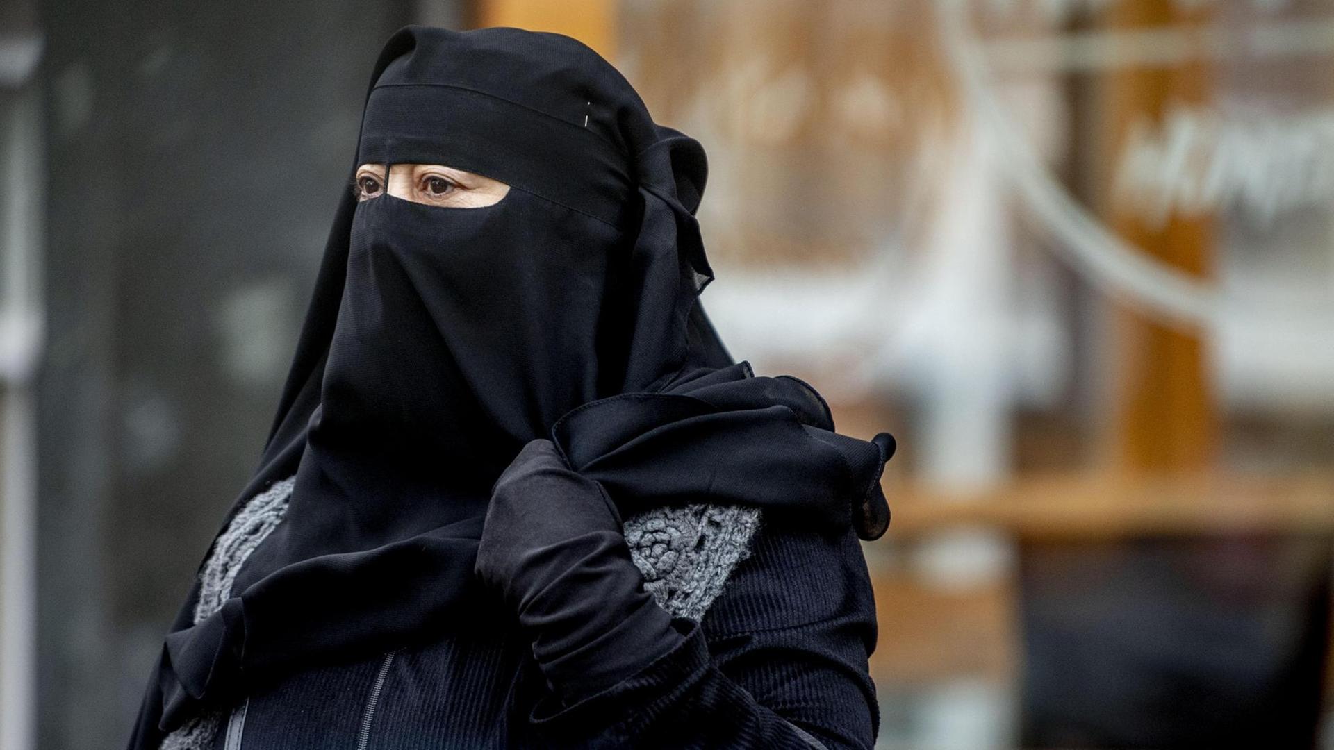 Zu sehen ist eine Muslima, deren Kopf bis auf die Augen mit einem schwarzen Tuch verhüllt ist. 