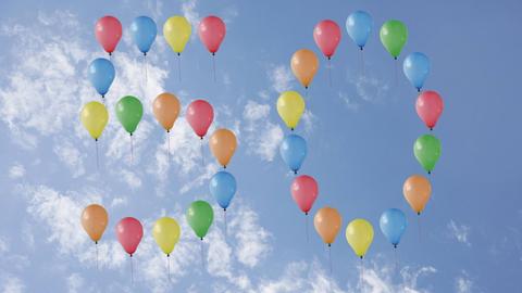 Bunte Luftballons bilden vor blauem Himmel die Zahl 50.