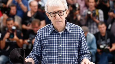Woody Allen sitzt an einem Tisch und hält einen Stoffhut in der Hand.
