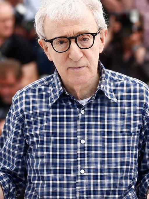 Woody Allen sitzt an einem Tisch und hält einen Stoffhut in der Hand.