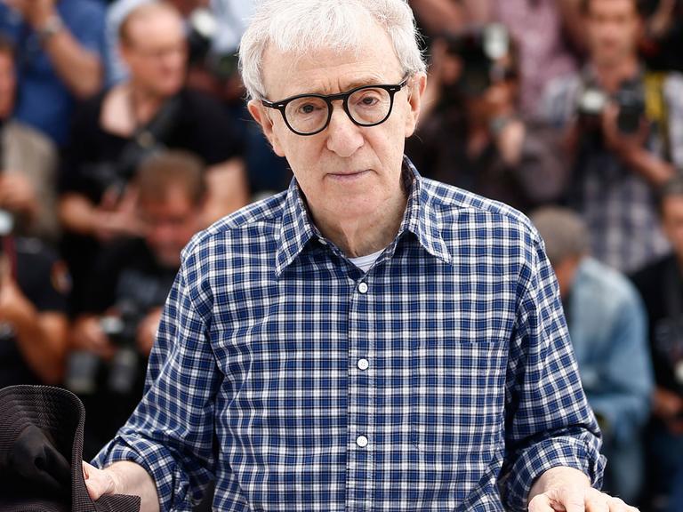 Woody Allen sitzt an einem Tisch und hält einen Stoffhut in der Hand.