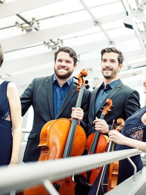 Die vier Musiker des Aris Quartett stehen unter einem Glasdach auf einer Rampe und halten die Instrumente in ihren Händen.