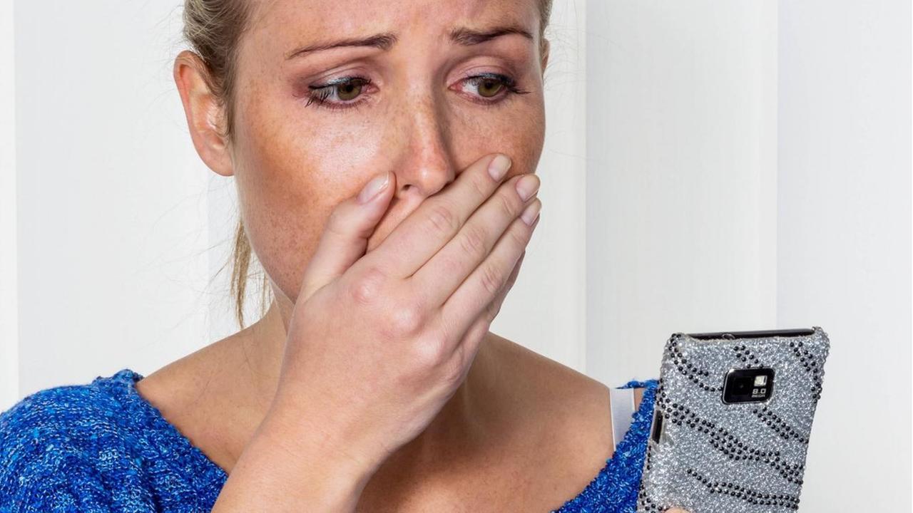 Eine Frau schaut auf ihr Handy und ist geschockt. Eine Frau schaut auf ihr Handy und ist geschockt.