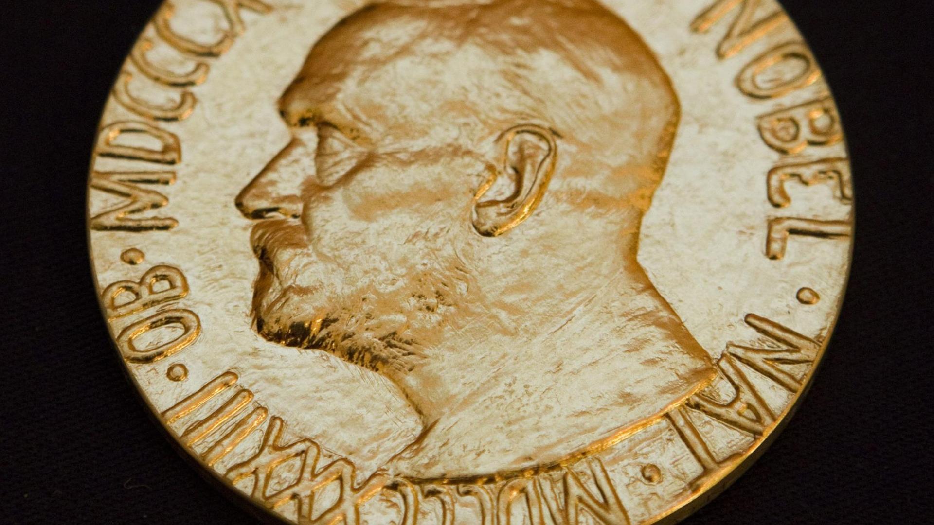 Eine goldene Medaille mit der Prägung des Profils von Stifter Alfred Nobel sowie am Rand dessen Geburts- und Todesdatum in römischen Ziffern