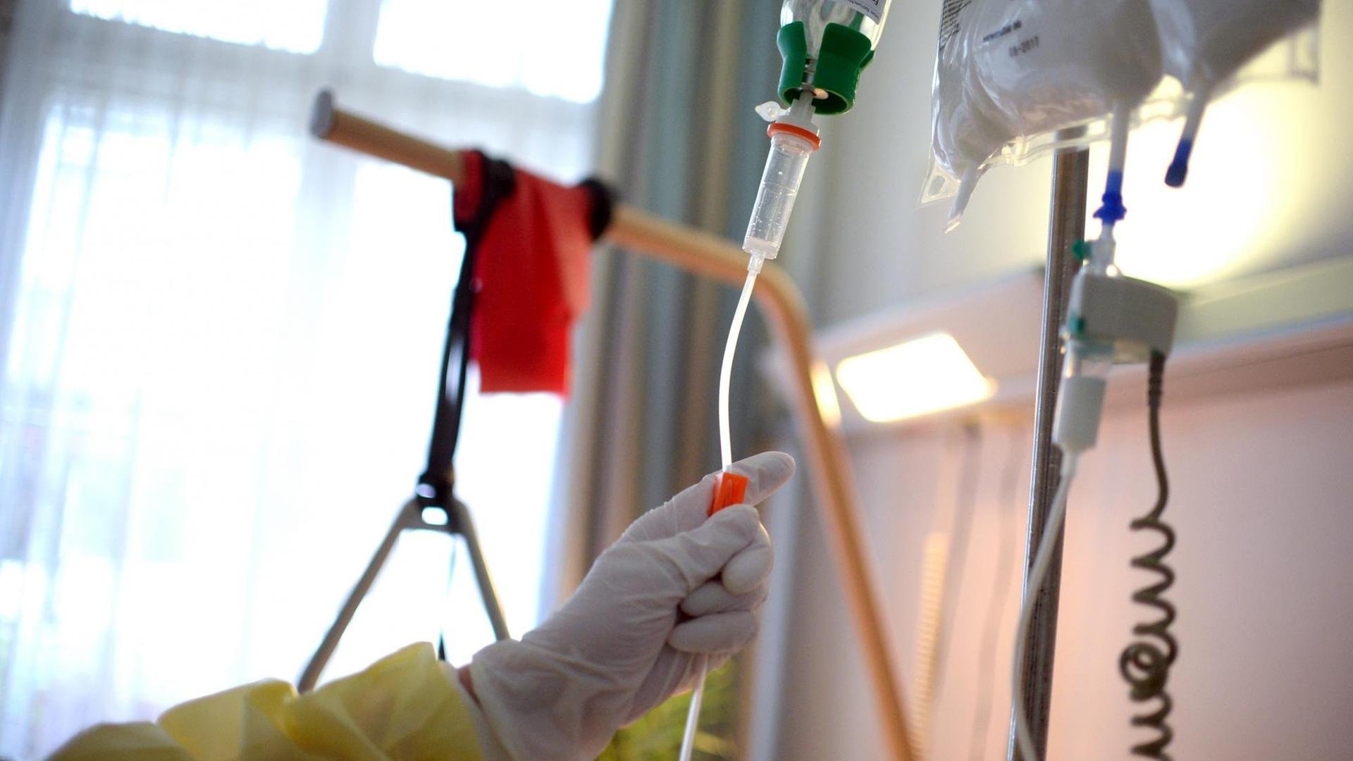 Eine Hand bereitet eine Infusion vor, die an einem Krankenbett befestigt ist.