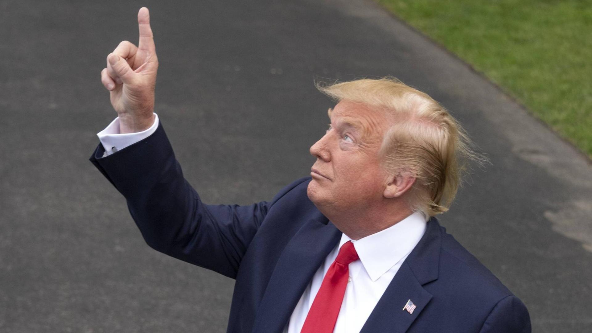 Donald Trump mit roter Kravatte, zeigt in den Himmel