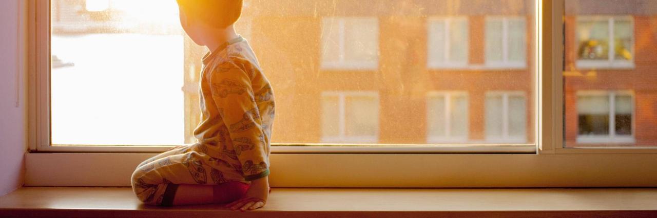 Ein Kind kniet auf einer Fensterbank und schaut aus dem Fenster. (Symbolbild)
