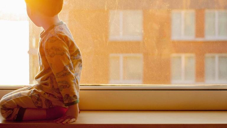 Ein Kind kniet auf einer Fensterbank und schaut aus dem Fenster. (Symbolbild) Ein Kind kniet auf einer Fensterbank und schaut aus dem Fenster. (Symbolbild)