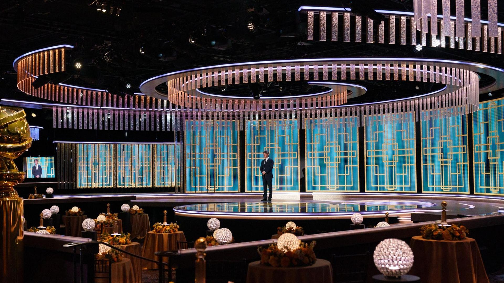 In einem Saal ohne Publikum steht ein Mann auf einer Bühne.