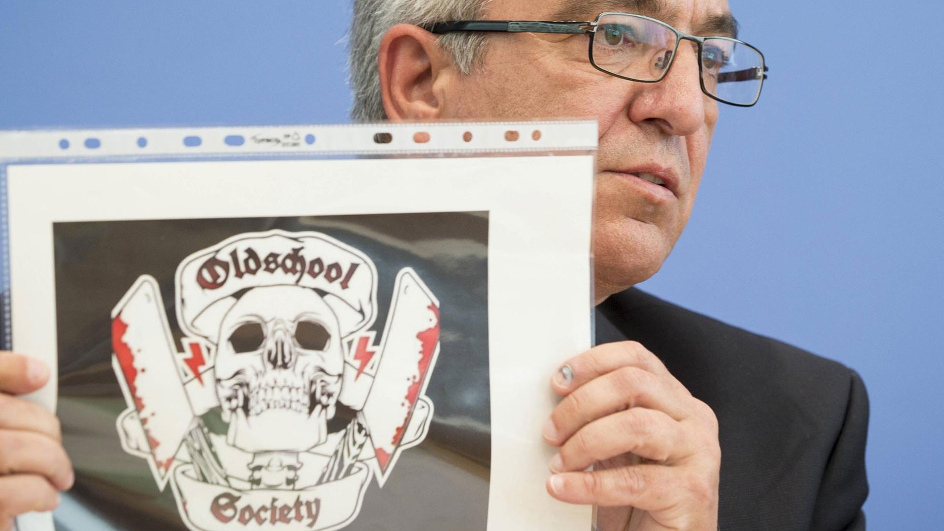 Der Vorsitzende der Innenministerkonferenz, Roger Lewentz, zeigt das Logo der rechtsextremen Gruppierung "Oldschool Society"