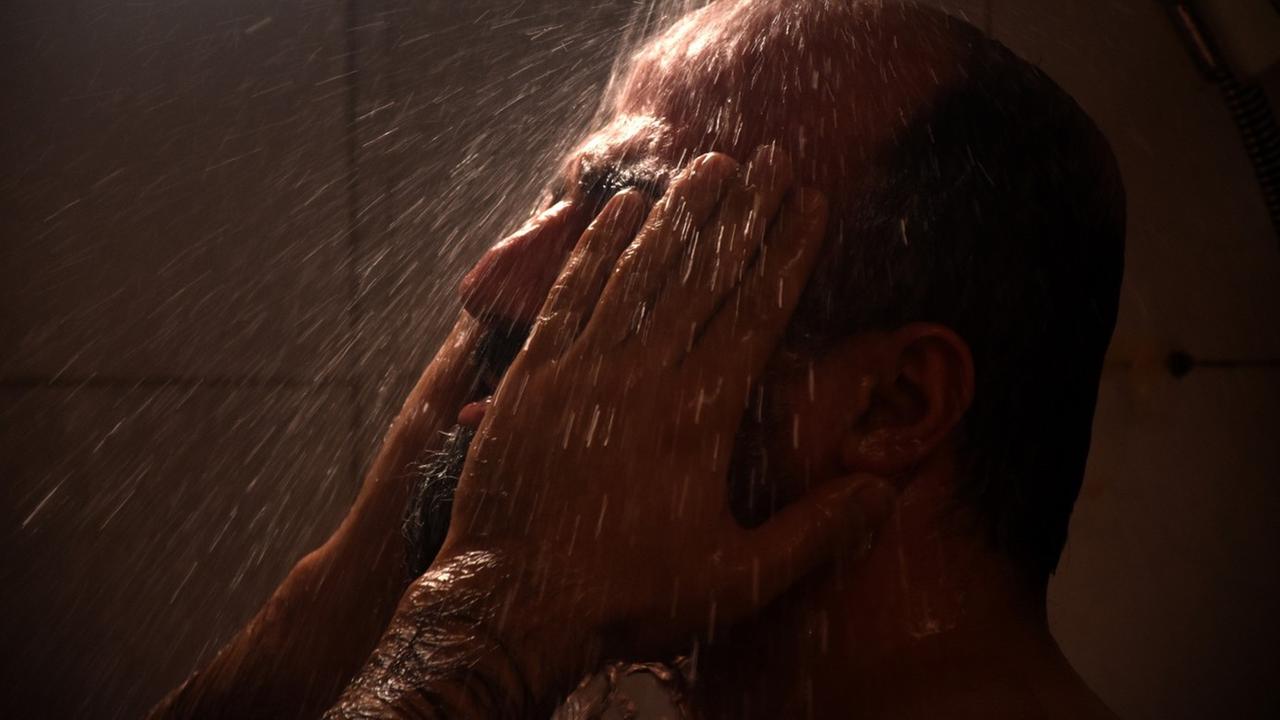 Im Still aus "Es gibt kein Böses" steht ein Mann unter der Dusche und hält sie die Hände vor sein Gesicht.