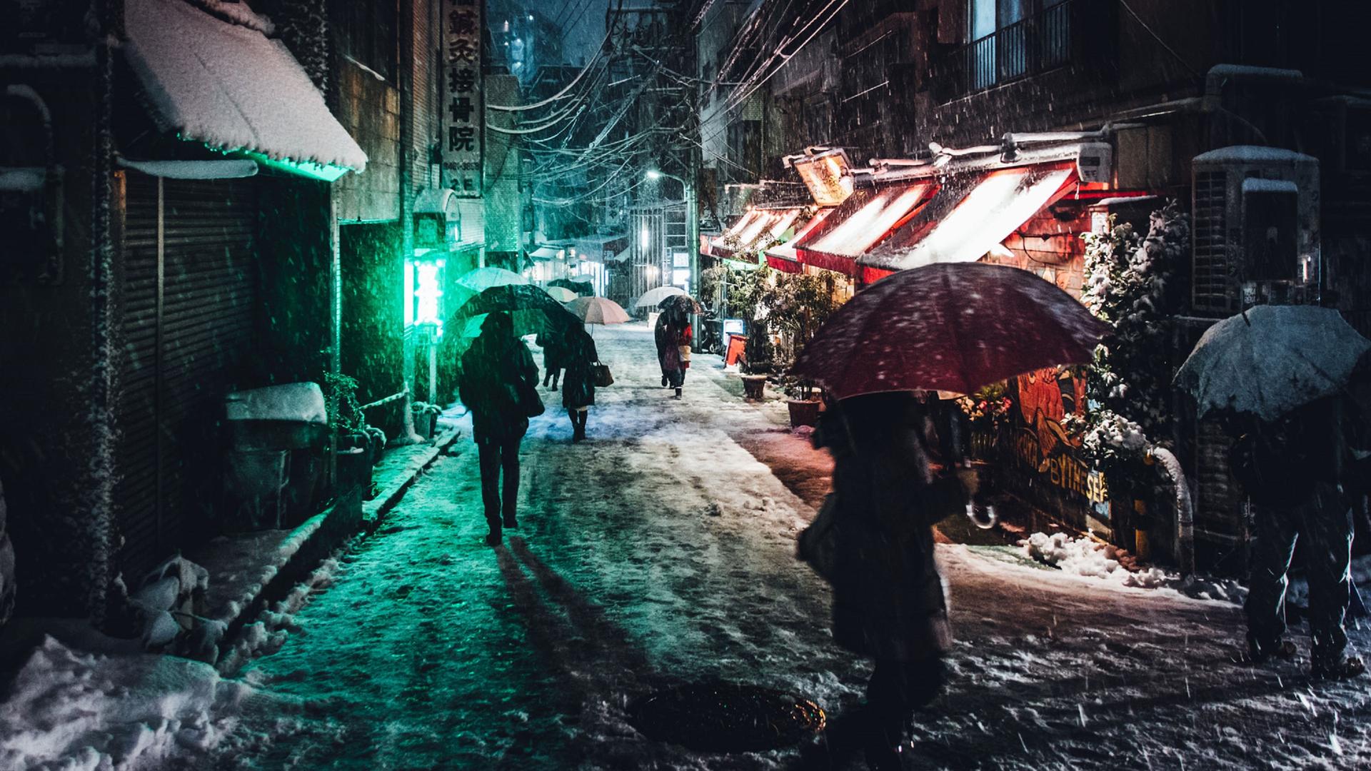 Menschen mit Regenschirmen gehen abends im Schirm durch eine kleine Straße in Tokio.