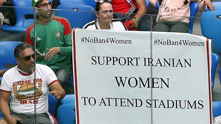 Das Bild zeigt eine Szene am Rande der Fußball-WM-Vorrundenbegegnung zwischen Marokko und dem Iran im Sankt-Petersburg-Stadion. Ein Poster zur Unterstützung von iranischen Frauen zum Besuch in Fußball-Stadien hängt an der Tribüne.