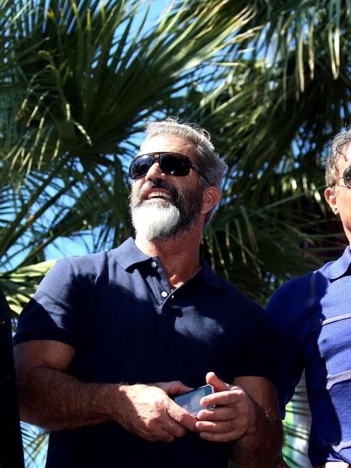 Harrison Ford, Mel Gibson und Sylvester Stallone stehen in Cannes vor Palmen.