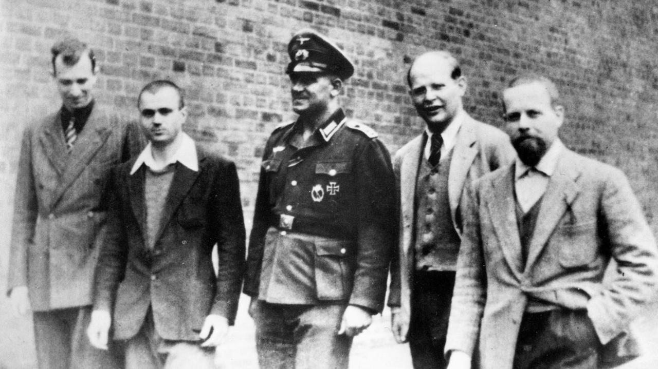 Das Schwarz-Weiß-Foto von 1944 zeigt Dietrich Bonhoeffer im Wehrmachtsgefängnis  Berlin-Tegel. Er steht in einer Reihe mit gefangenen Offizieren der italienischen Luftwaffe und einem Wehrmachtsoffizier. V.l.n.r. Mario Gilli, Dante Curcio, Oberfeldwebel Napp, Bonhoeffer, Edmondo Tognelli. 