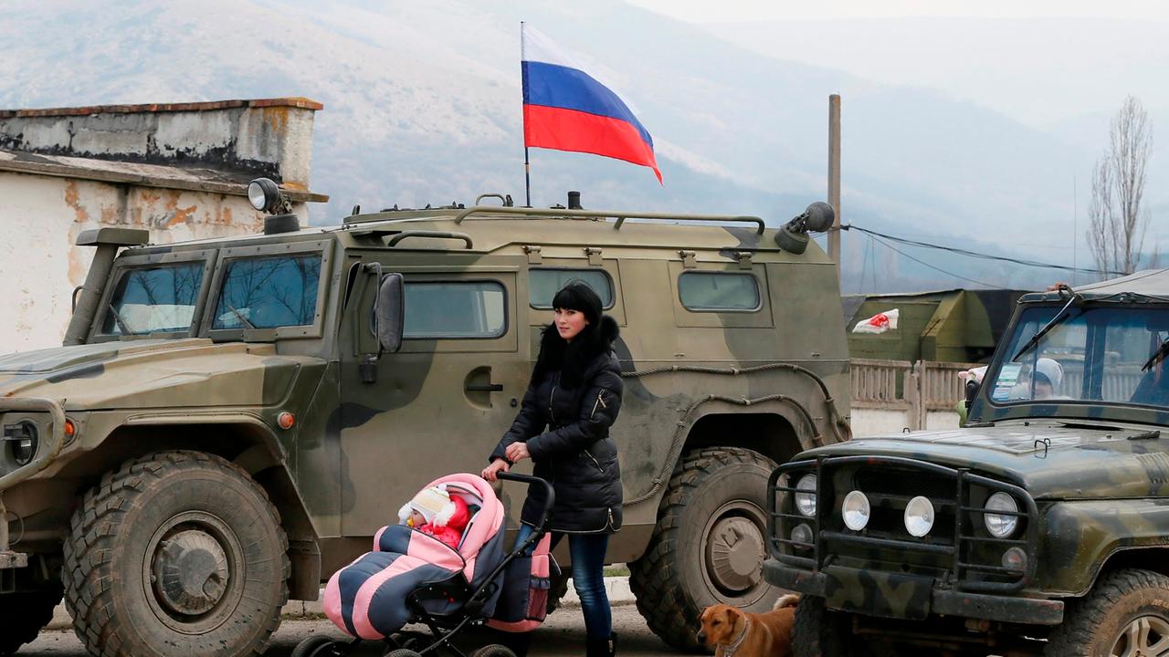 epa04121671 A woman walks with her baby in front of Russian 'GAZ Tigr' infantry mobility vehicle outside the territory of Ukrainian military unit in the village of Perevalnoye, outside Simferopol, Ukraine, 12 March 2014. Crimea's secessionist authorities 