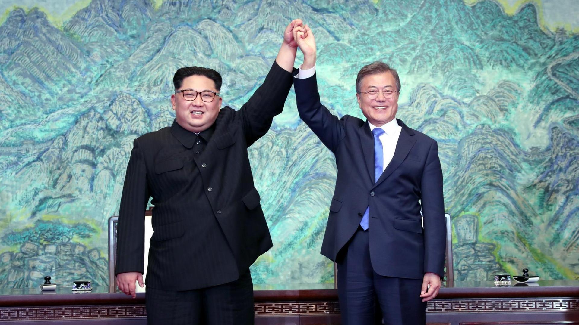 Kim Jong-un un Moon Jae-in halten sich bei ihrem Treffen in Panmunjom an den Händen und diese in die Luft