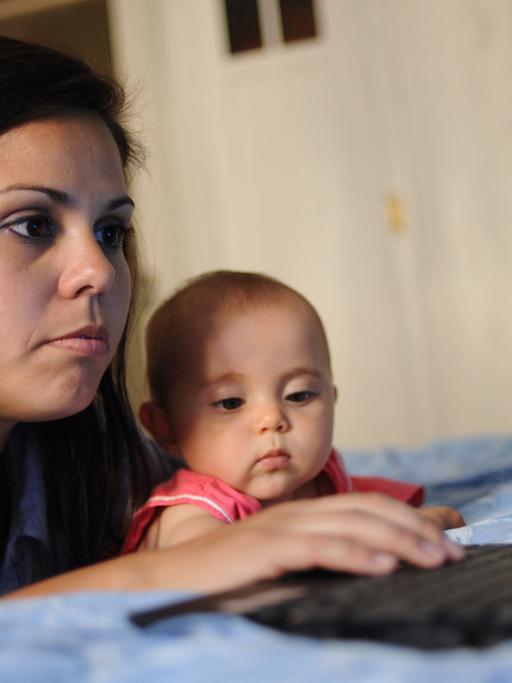 Eine Frau liegt am 10.6.2010 in ihrer Wohnung auf dem Bett und schaut auf einen Computerbildschirm, während ihre acht Monate alte Tochter daneben liegt und zuschaut.