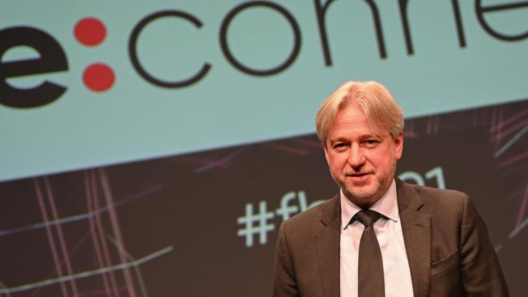 Juergen Boos, Direktor der Frankfurter Buchmesse, steht nach der Eröffnungspressekonferenz der Buchmesse vor einer Projektion des Buchmesse-Titels "Re:connect".